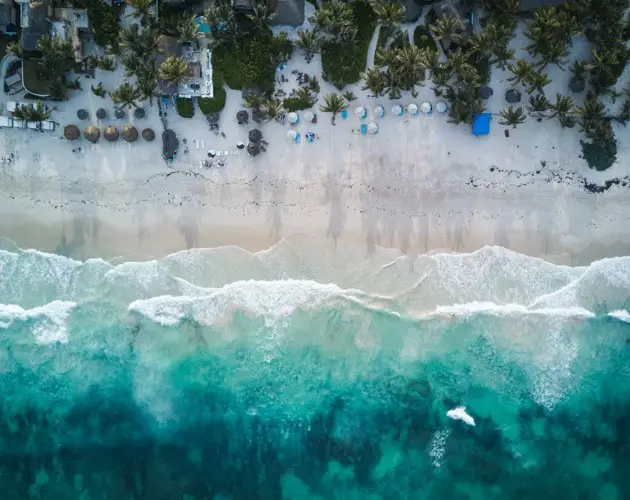 Luftaufnahme eines Strandes mit klarem Wasser und sanften Wellen in einer tropischen Umgebung.
