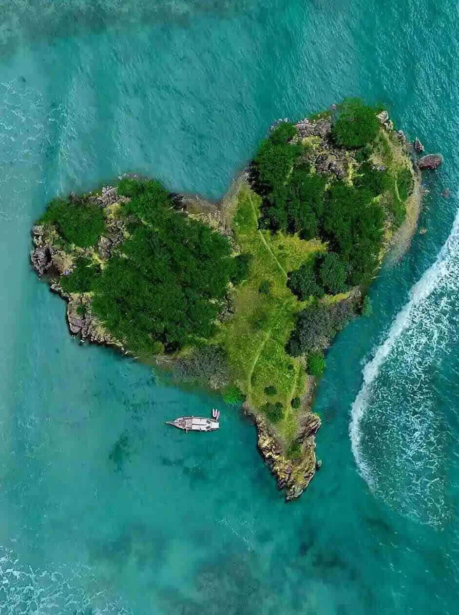 Aerial view of a lush green tropical island surrounded by turquoise sea, sandy beach, and white waves along the shore.